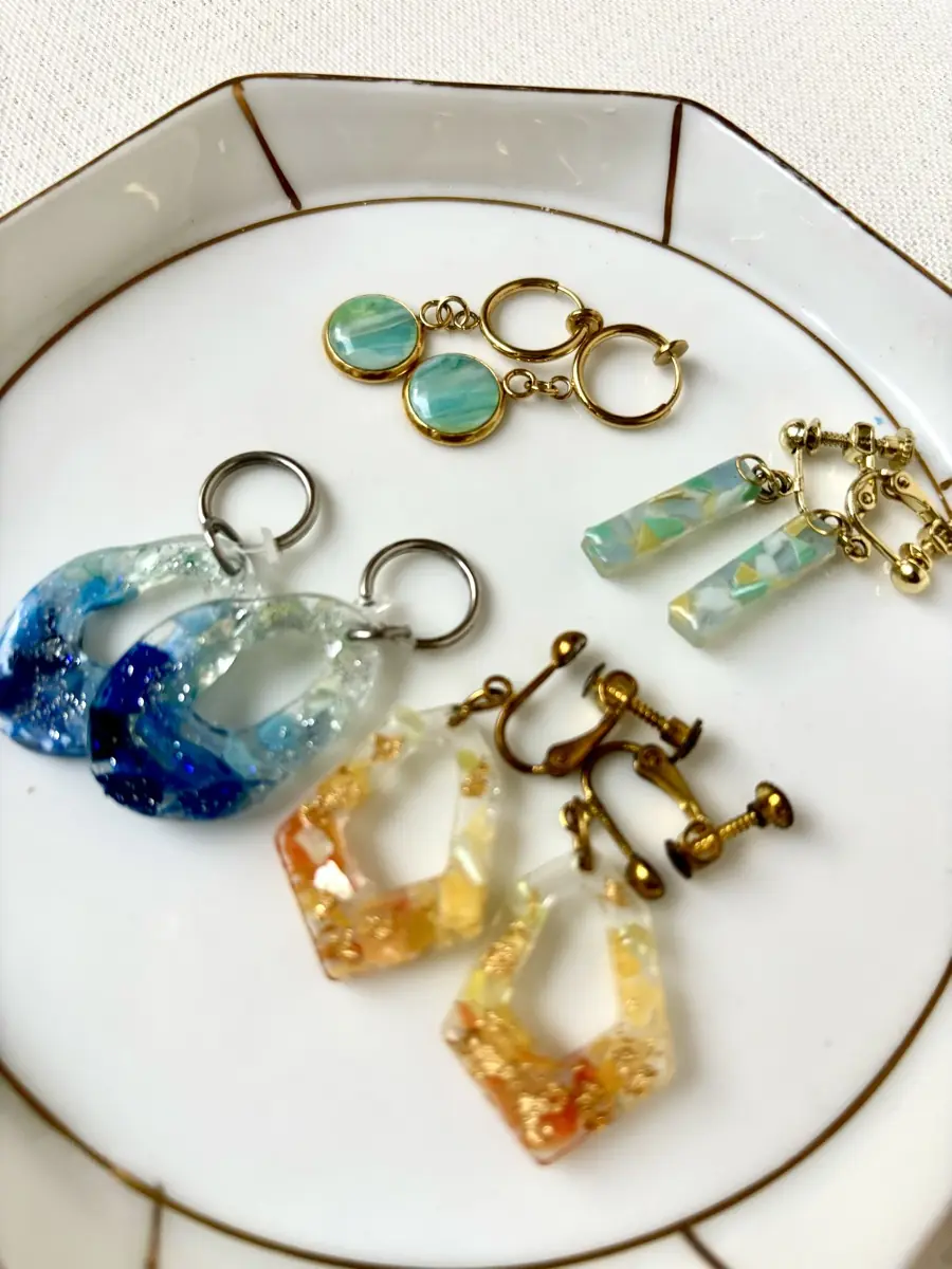 水晶樹脂に海のカケラを封じた完成作品。イヤリングとチャームを白い皿に並べたところ