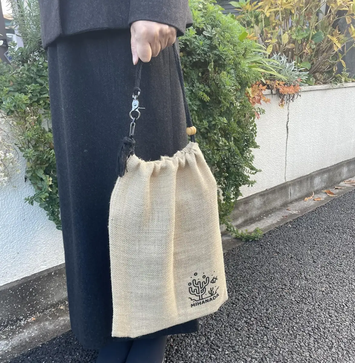 黒いコートの装いに合わせて、み*はなだポーチを手に提げて住宅街を歩く様子