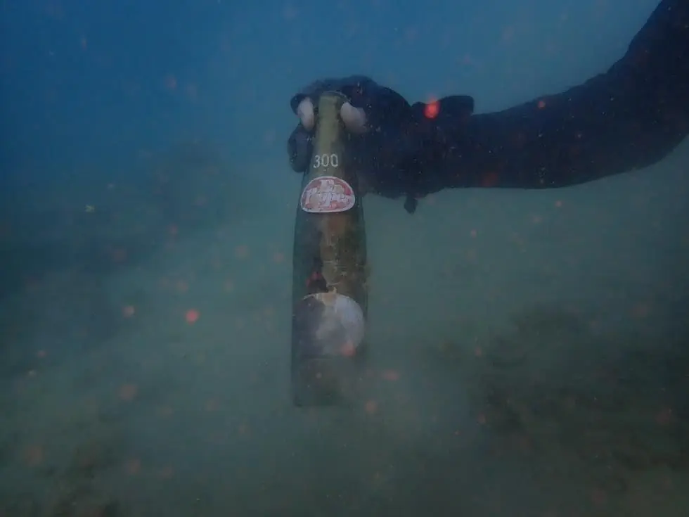 海底から拾い上げられた古い瓶をグローブの手で持つダイバー