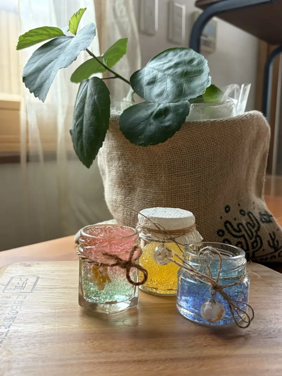麻ひもを結んだ小瓶3つ。ピンク・黄・青の中身に、海のカケラのチャームを添えたもの